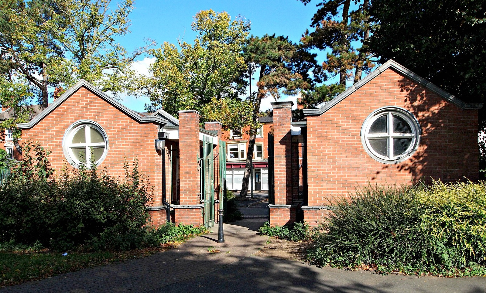 Brick entrance lodges and gateway to Southfields Park, Loughborough, framed by trees and shrubs on a sunny day.