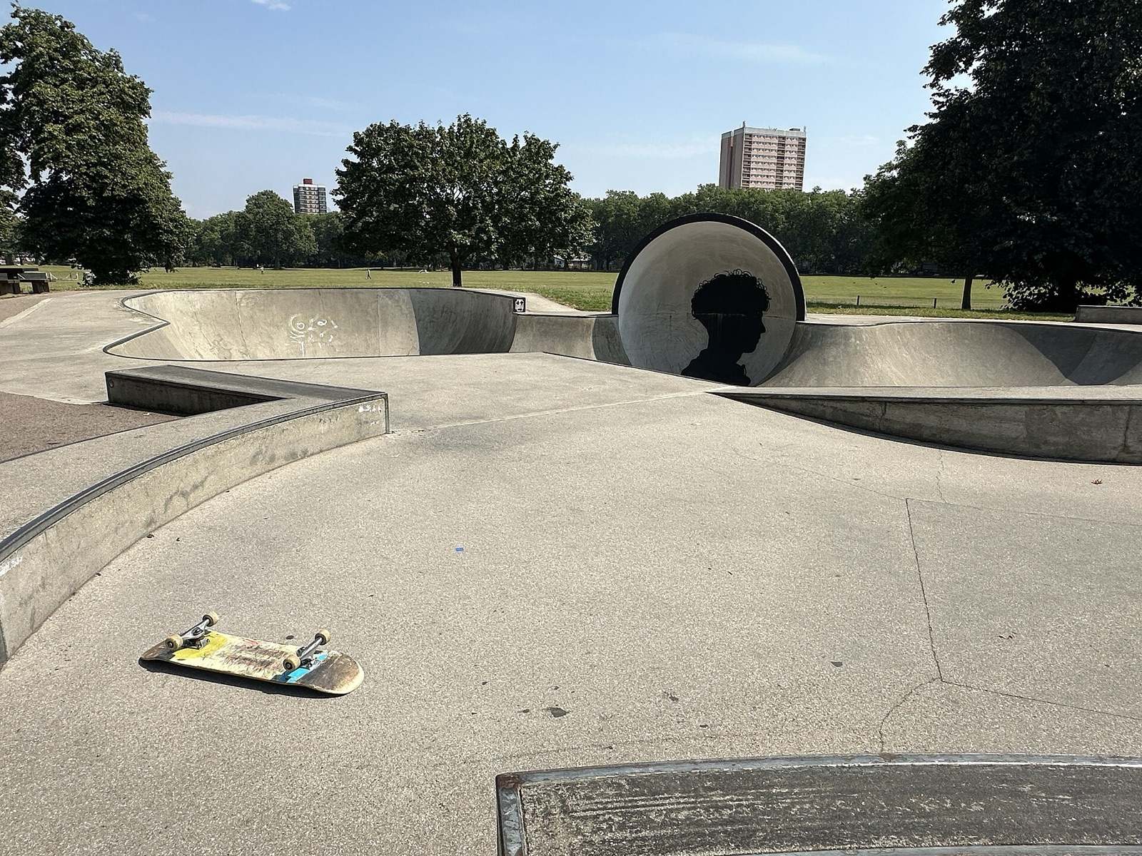 A smooth concrete skatepark in Victoria Park, London, with bowls, banks and a round sculpture under a clear sky.